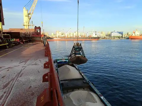 A ship’s crane and grab working a barge loaded with salt in the harbor