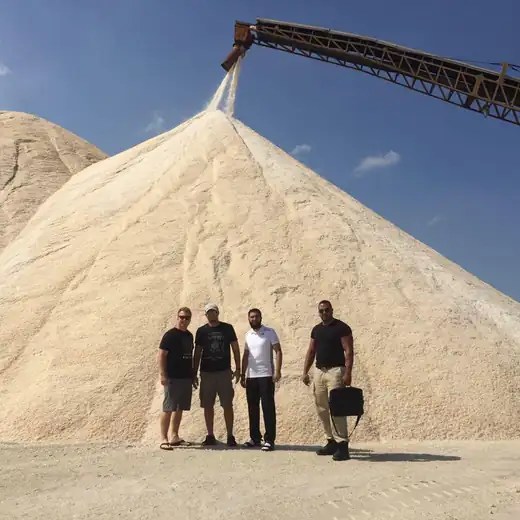 Bulk salt stockpile being built by a stacker conveyor, with four people standing at its base for scale